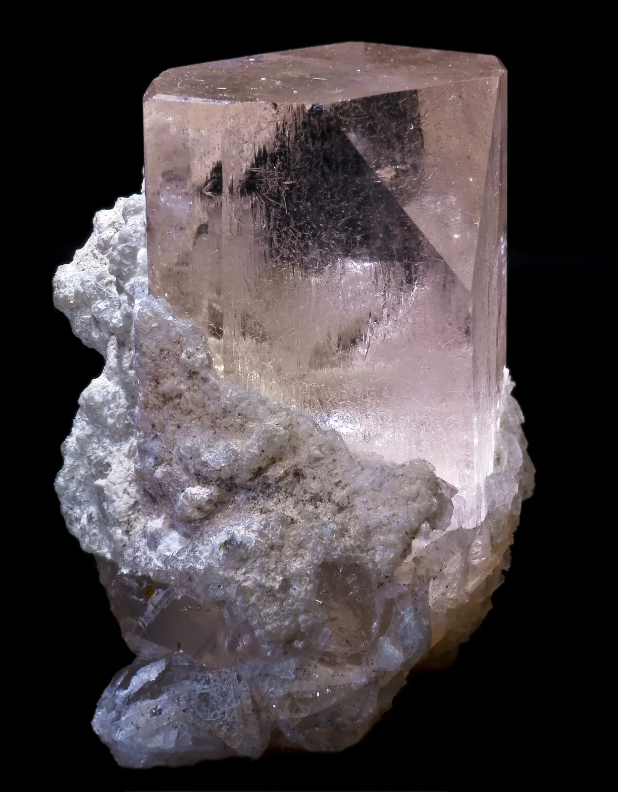 Mittlerer rosa Topas-Kristall auf weißer Mineralmasse mit schwarzem Hintergrund.