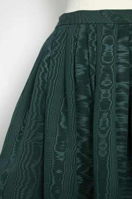 Fotografía conceptual de primer plano de una falda verde de popelín con pliegues y textura visual detallada.