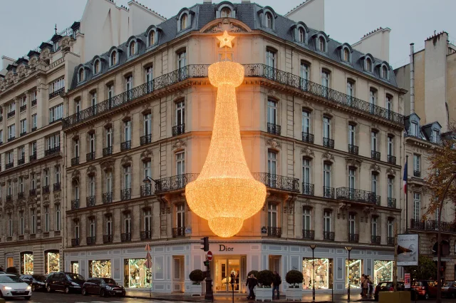 Imagen conceptual de la tienda Dior en 30 Avenue Montaigne en París, Francia, con decoración iluminada en forma de estrella y lámpara gigante en la fachada del edificio histórico.