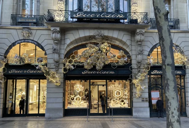 Vitrina de Navidad de la boutique Guerlain en los Campos Elíseos, con decoraciones doradas y luces festivas.