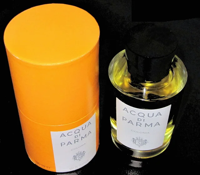 Imagen conceptual que muestra una botella de Acqua di Parma Colonia Eau de Cologne junto a su empaque cilíndrico amarillo característico, sobre un fondo negro.